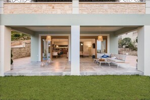A modern house with a stone facade, a covered patio with outdoor furniture, and a visible kitchen area. - Erato Villa in Gavalochori (Apokoronas)