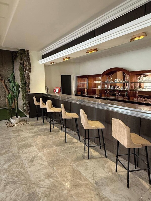 A bar area with a long counter, multiple stools, and a display of glassware. - Treehouse Hotel (Sousse)