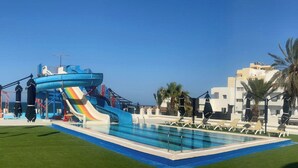 A swimming pool with a water slide, lounge chairs, and palm trees.
