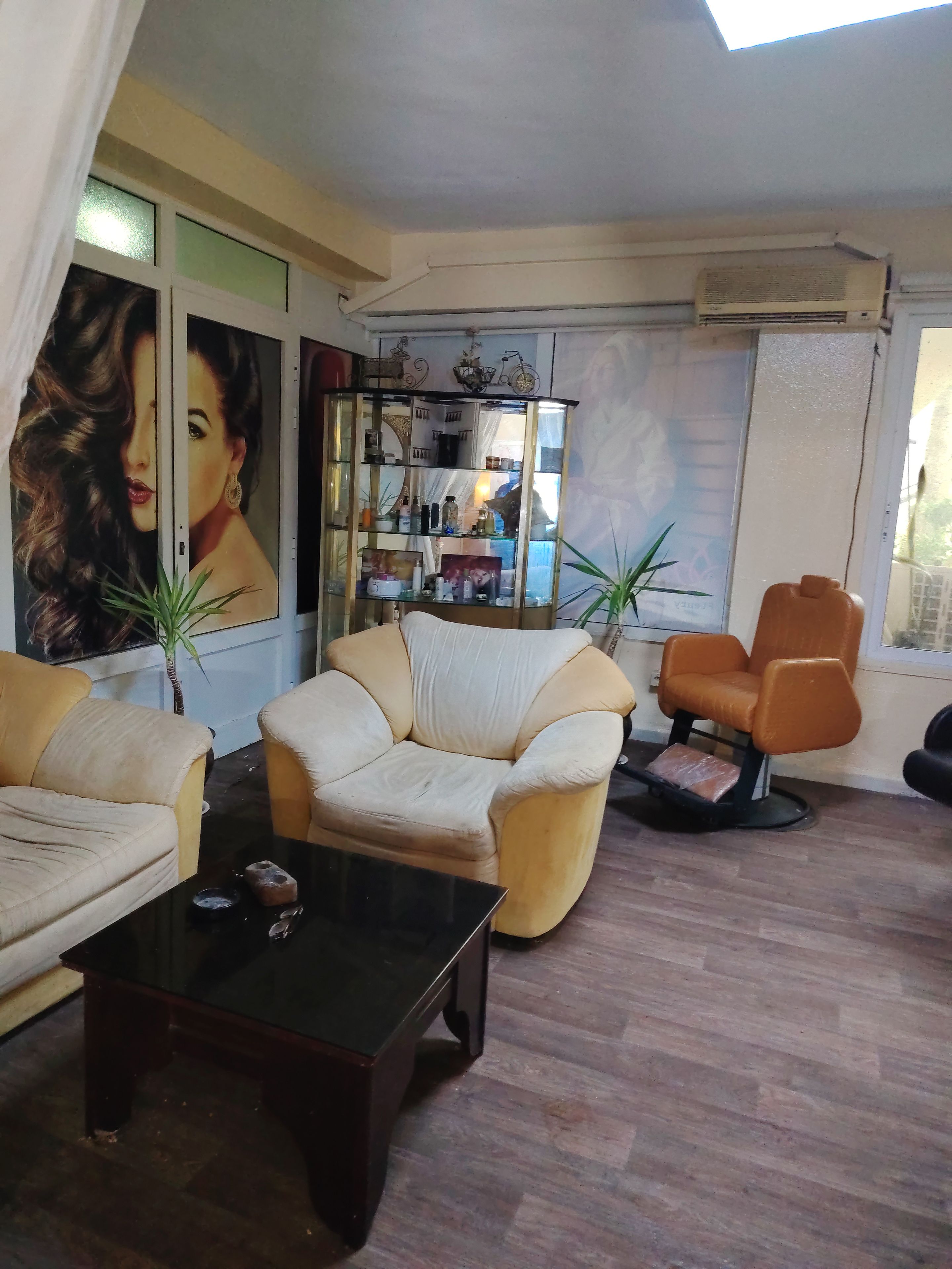 Un salon comprenant un canapé, un fauteuil et une table basse. On y trouve une bibliothèque avec des objets décoratifs et une grande fenêtre avec des rideaux.
