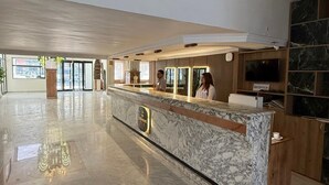 Un hall d’entrée spacieux avec un comptoir de réception en marbre, un espace d’accueil et une grande fenêtre laissant entrer la lumière naturelle.