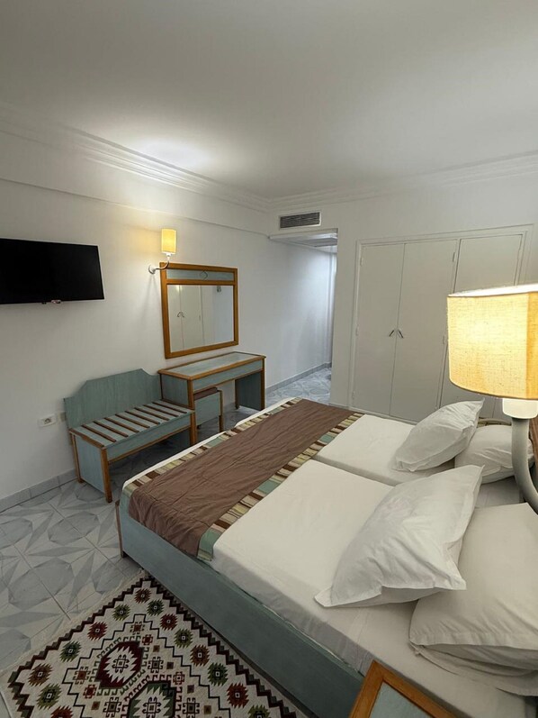 A hotel room with two beds, a desk, a chair, a TV, and a wardrobe. - Treehouse Hotel (Sousse)