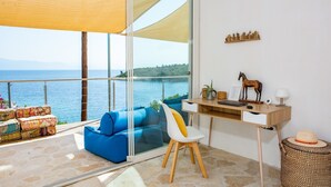 Un balcon avec vue sur la mer, un canapé bleu, un bureau en bois et un panier en osier.
