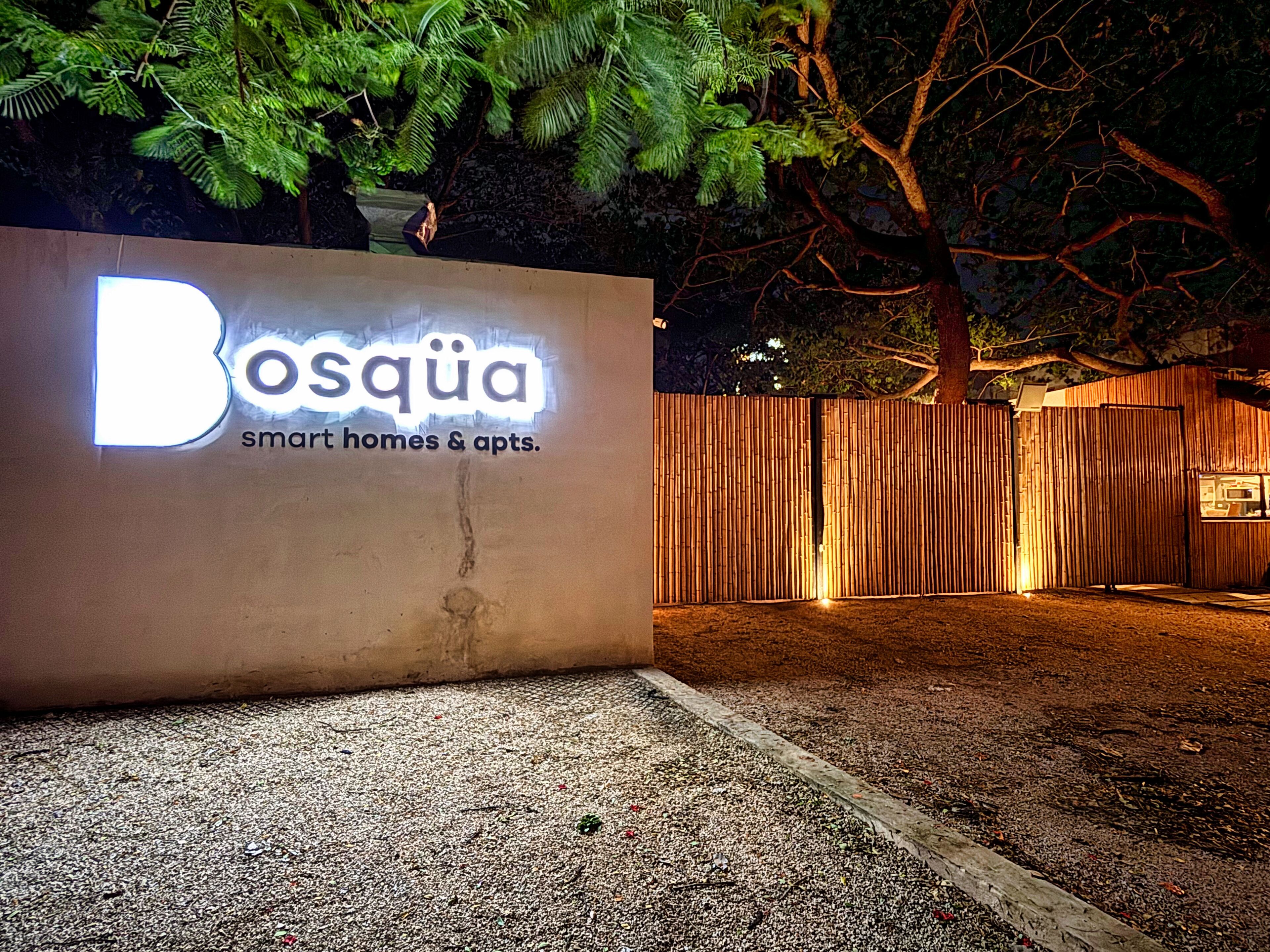 A sign for 'Bosqua smart homes & apartments' with a bamboo fence and trees in the background.