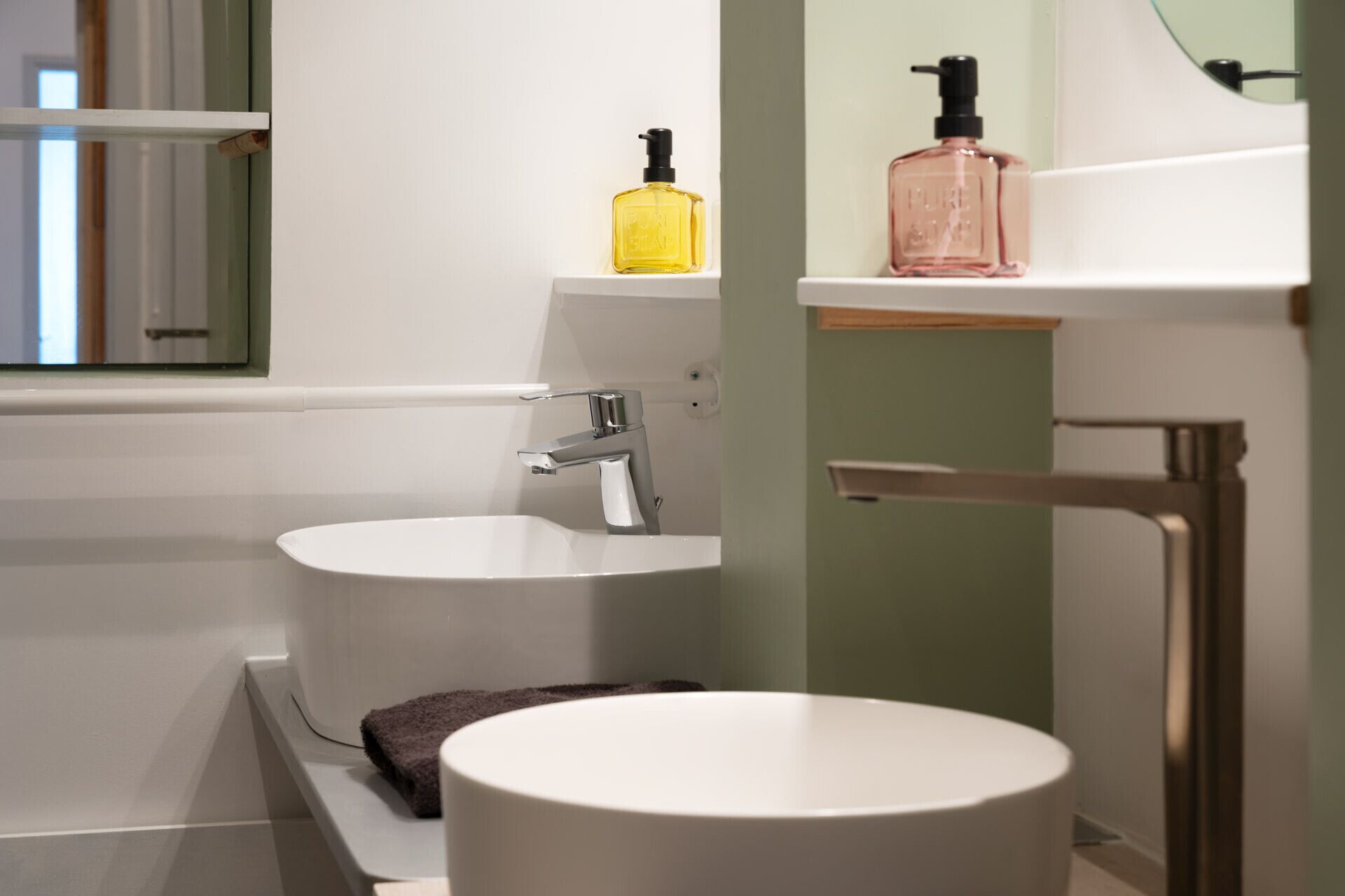 Un bagno moderno con un lavandino bianco, uno specchio rotondo e un soffione doccia a mano.