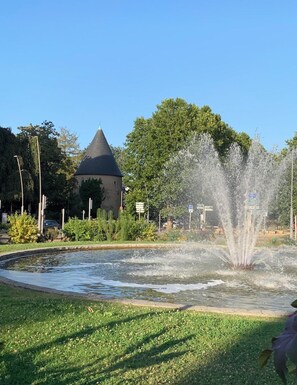 A fountain with water jets, a grassy area, and a building with a conical roof. - Mondon 3 Arcades – 3 Bedrooms, 2 Showers, Up to 8 G (Metz)