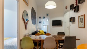 Een moderne woonkamer met een eethoek, met een grote spiegel, kunstwerken aan de muur en een flatscreen televisie.