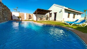 A swimming pool with a stone wall, a covered patio, and lounge chairs.