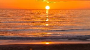 A sunset over a beach with waves and a clear sky.