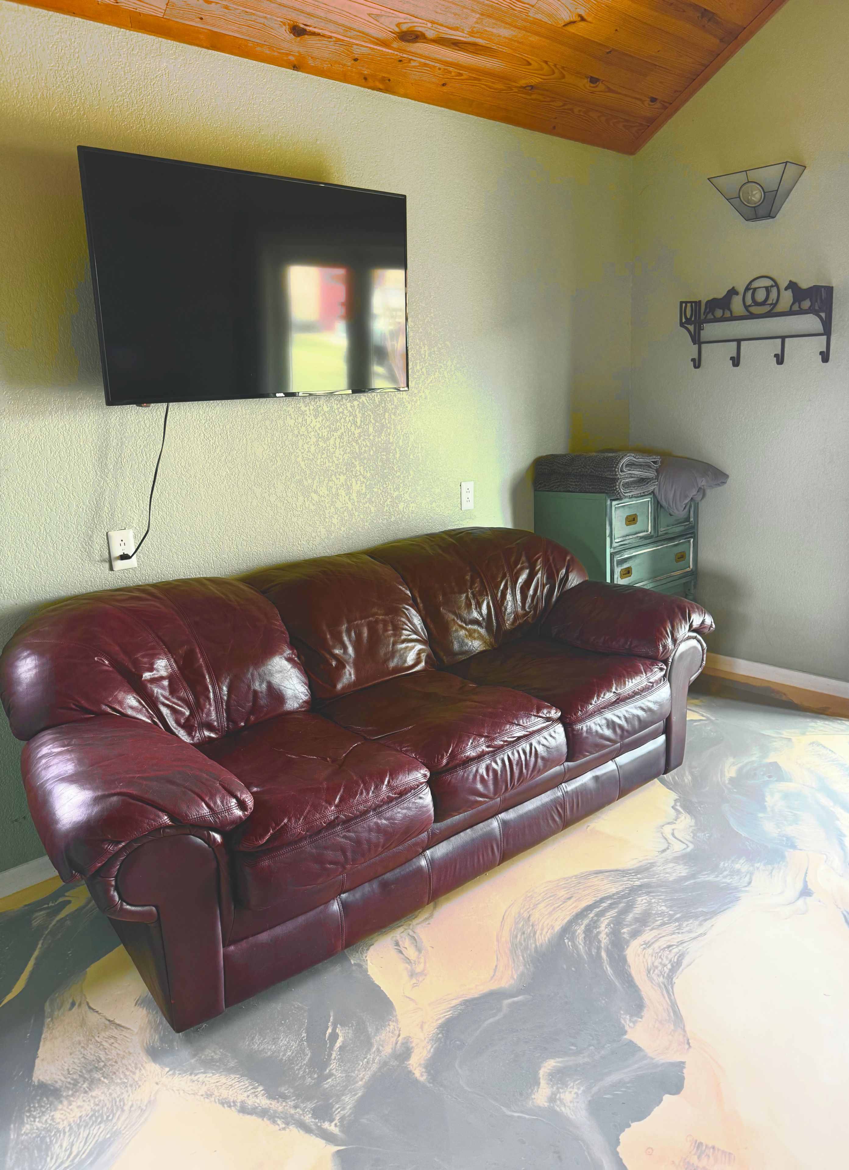 Une pièce comprenant un canapé en cuir, un téléviseur fixé au mur, un luminaire mural et un élément décoratif en métal.