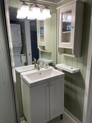 A bathroom with a white sink, mirror, and vanity. There is a shelf above the mirror and a window with a floral pattern. - Entire guesthouse in New Braunfels, Texas (New Braunfels)