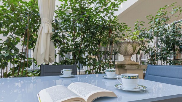 An outdoor seating area with a table, chairs, a book, and a decorative urn. - Prestige Apartment Via Roma by Wonderful Italy (Turin)