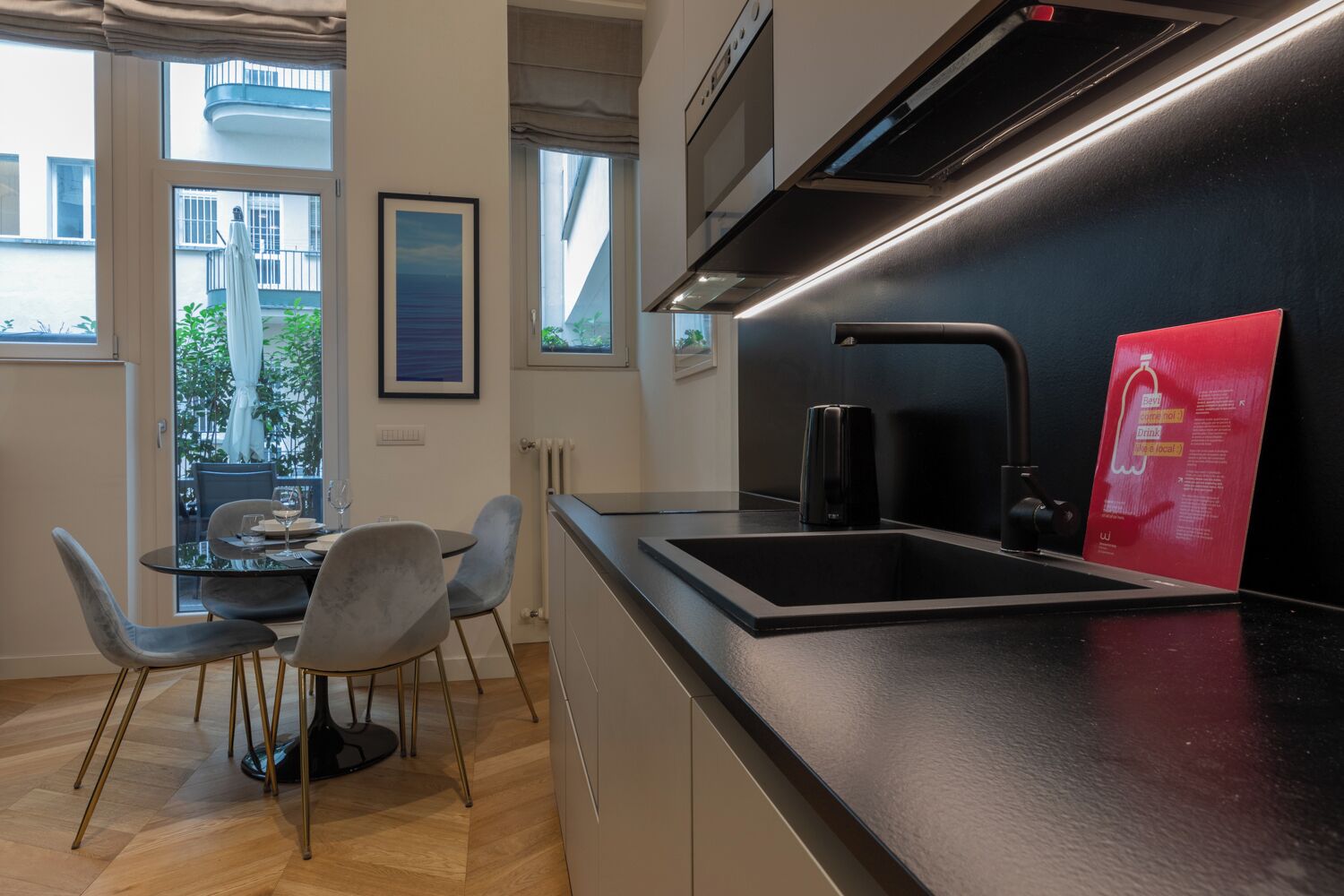 Una cocina moderna con encimera negra, pileta de acero inoxidable y un cartel informativo rojo.