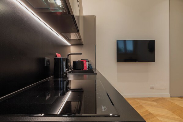 A modern kitchen with a black induction cooktop, a built-in oven, and a flat-screen TV mounted on the wall. - Prestige Apartment Via Roma by Wonderful Italy (Turin)