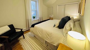 Et soveværelse med seng, skrivebord, stol, loftventilator, et vindue med gardiner og en sengetøjslampe.