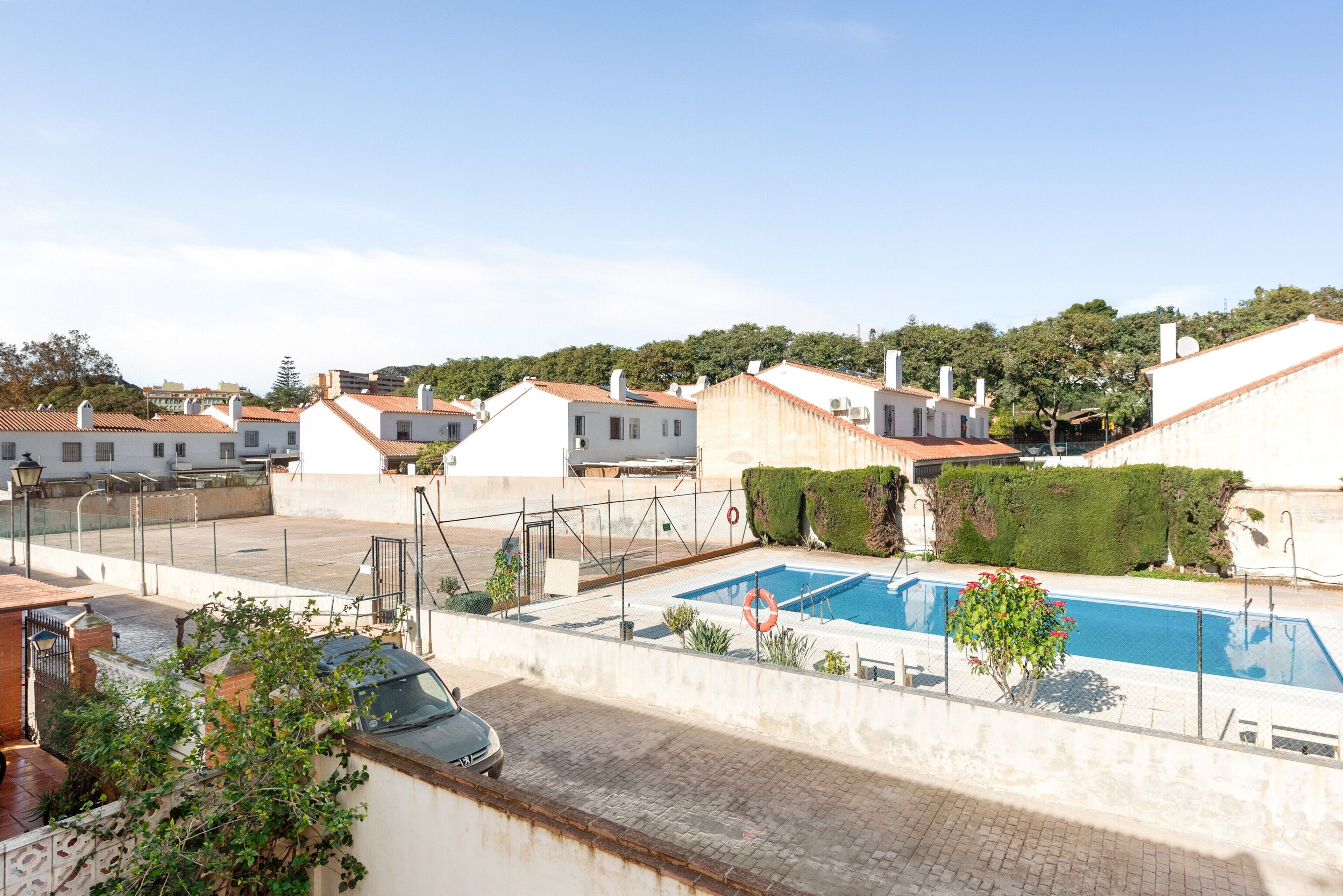 Zona residencial con piscina, casas de techo en tejas rojas y un coche estacionado al frente.