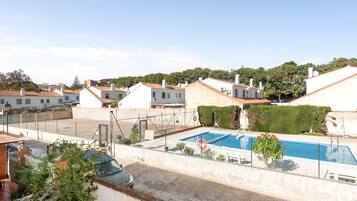 Zona residencial con piscina, casas de techo en tejas rojas y un coche estacionado al frente.