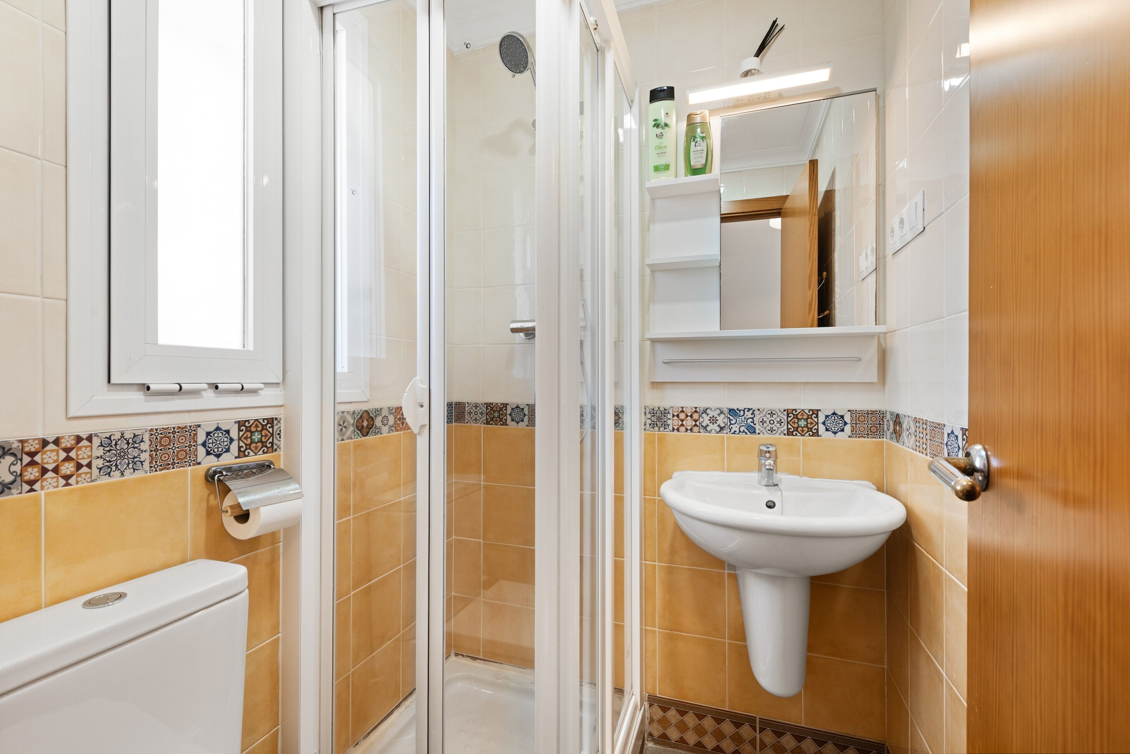 A bathroom with a toilet, shower, sink, and a mirror.
