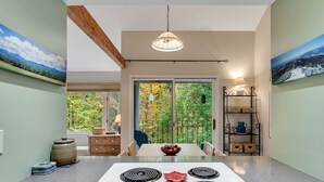 Une cuisine moderne dotée d’un îlot central, d’un coin repas offrant une vue sur les arbres et d’un balcon avec une balustrade.