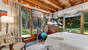 A spacious bedroom with a large bed, exercise equipment, a television, and a view of the outdoors.