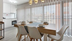 A modern dining area with a wooden table, white chairs, and hanging pendant lights. - Coral Beach Apartment (Figueira da Foz)
