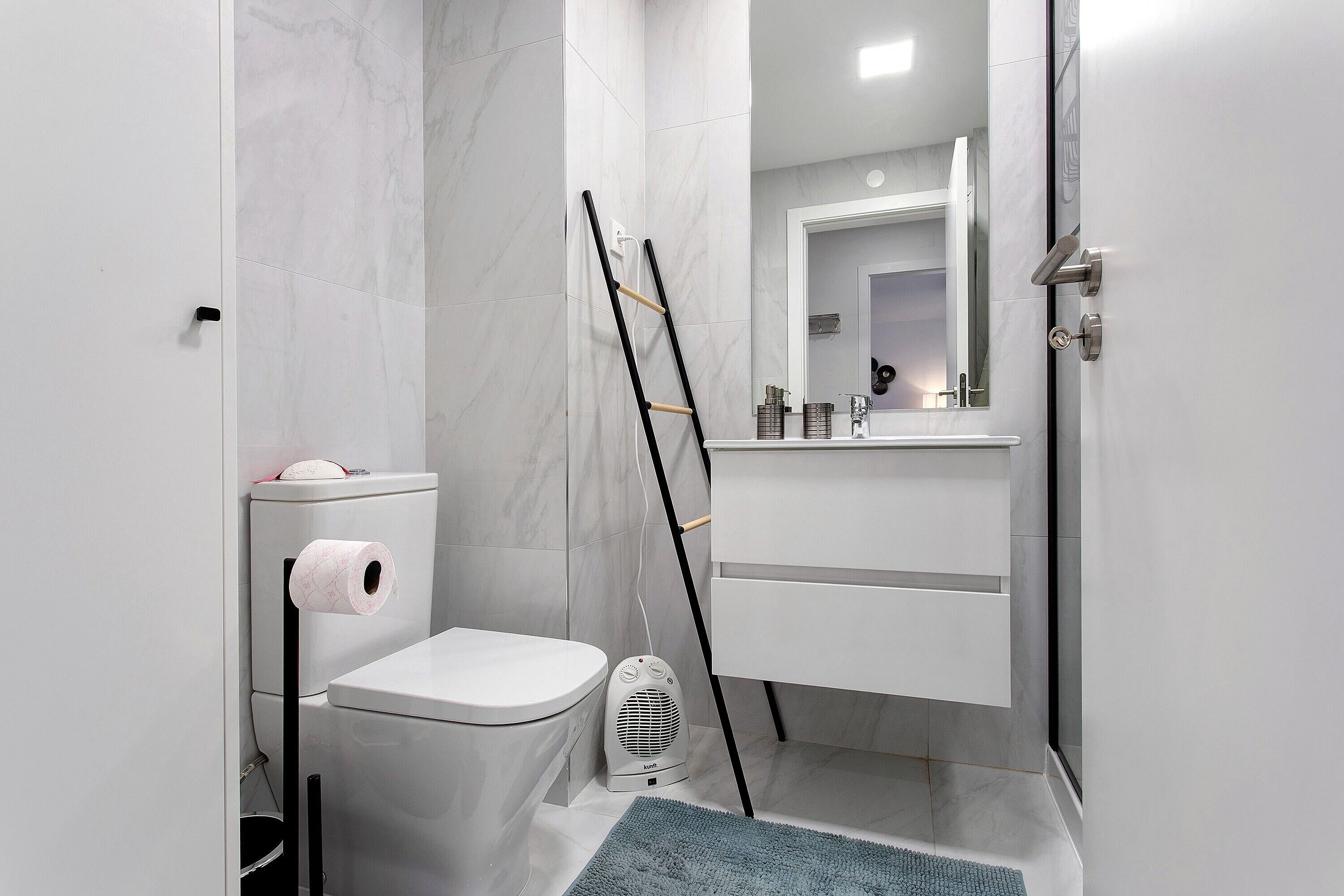 Ein Badezimmer mit Toilette, einem Händetrockner, einem Spiegel und einem Handtuchhalter.