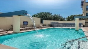 Ein Schwimmbecken mit Wasserspiel, Liegestühlen und einem Gebäude im Hintergrund.