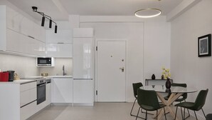 A modern kitchen with white cabinets, a microwave, and a dishwasher. There is a dining area with a glass table and green chairs. - Charitos Luxury Hideaway 2bd Apt in Kolonaki (Athina)
