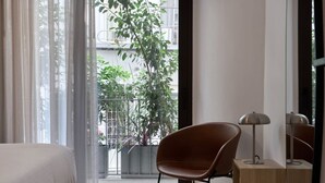 A modern bedroom with a large window, a brown chair, a bedside table, and a lamp. - Charitos Luxury Hideaway 2bd Apt in Kolonaki (Athina)