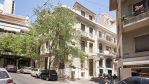 A street view with parked cars, a tree, and buildings with balconies and signage. - Charitos Luxury Hideaway 2bd Apt in Kolonaki (Athina)