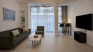 A modern living room with a sofa, a coffee table, a TV, and a dining area with chairs. - Charitos Luxury Hideaway 2bd Apt in Kolonaki (Athina)