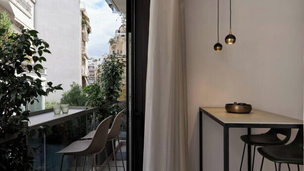 A balcony with a table and chairs, a hanging light fixture, and a view of the cityscape. - Charitos Luxury Hideaway 2bd Apt in Kolonaki (Athina)