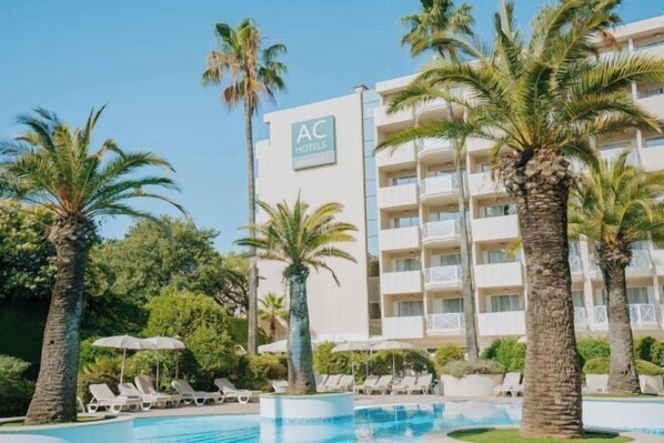 Ein Hotel mit Poolbereich, Palmen und Liegestühlen.