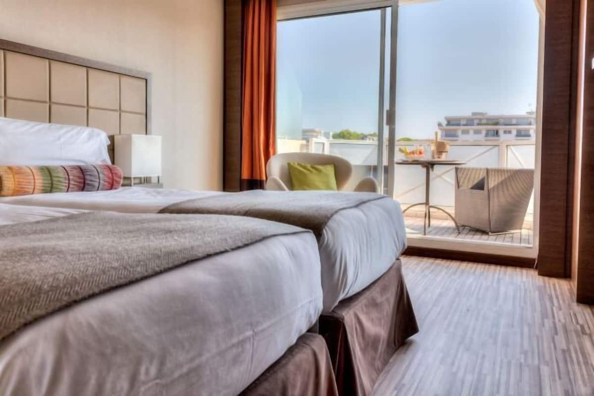 Quarto de hotel com uma cama grande, uma cadeira, uma mesinha e varanda com vista.