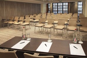 Une salle de conférence avec des rangées de chaises, une longue table couverte de papiers et de stylos, et de grandes fenêtres.