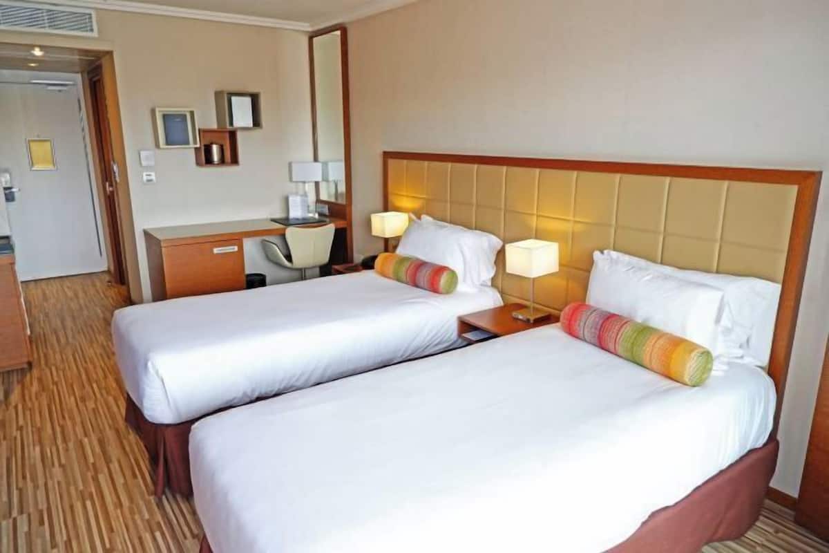 Quarto de hotel com duas camas, uma escrivaninha e uma cadeira.