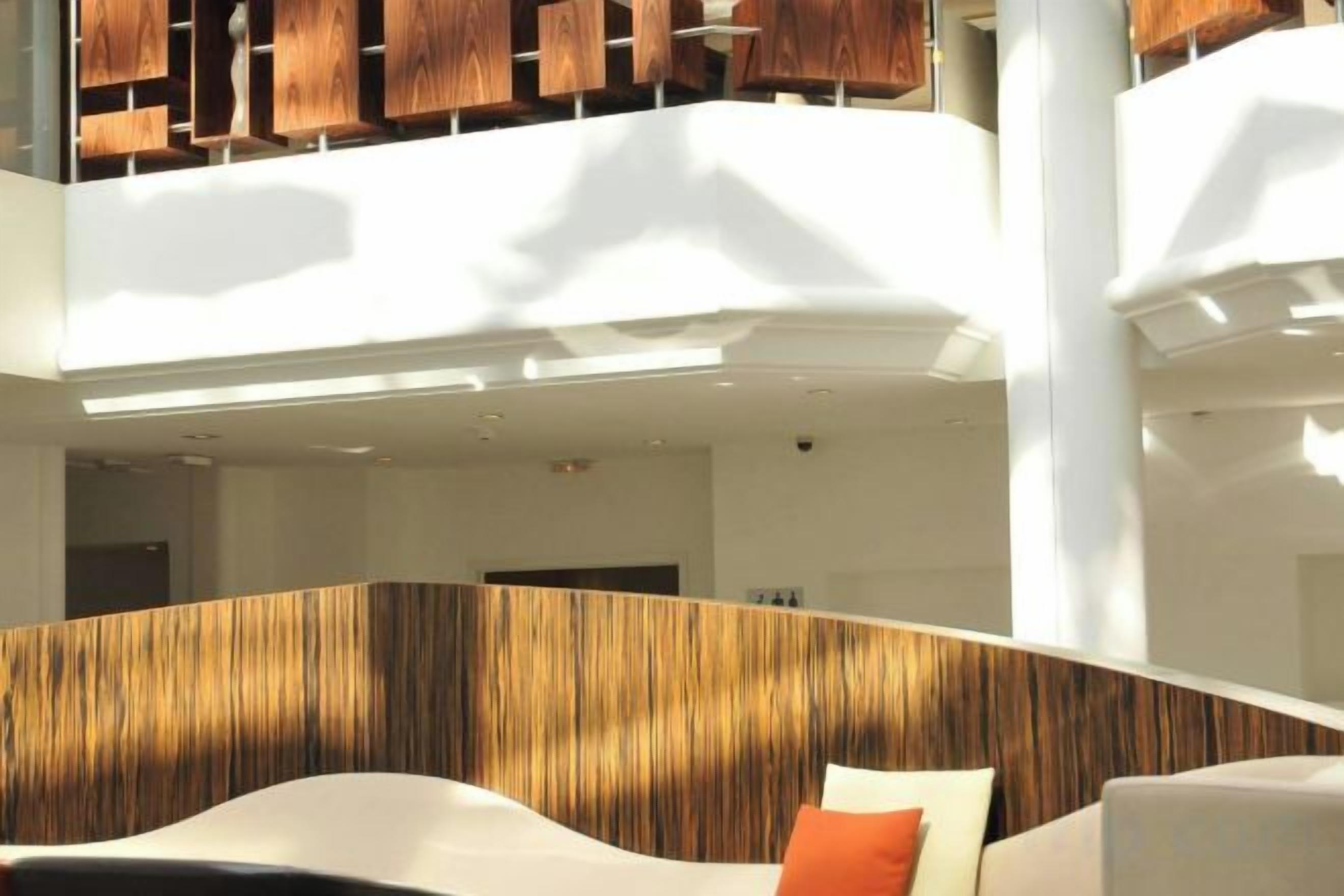 Un interior moderno con una pared curva, una zona de estar con cojín y una escalera visible.