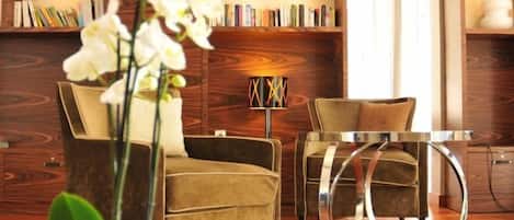 A modern living room with a sofa, armchair, and a glass coffee table. There is a bookshelf with books and decorative items.