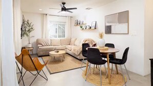 En moderne stue med sofa, spisebord med stole, ventilator og et stort vindue.