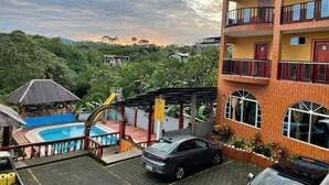 Un hotel con piscina, zona techada y un coche estacionado frente a él.