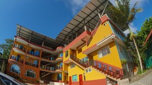 Un edificio de varios pisos con fachada roja y amarilla, balcones y un acceso cubierto.