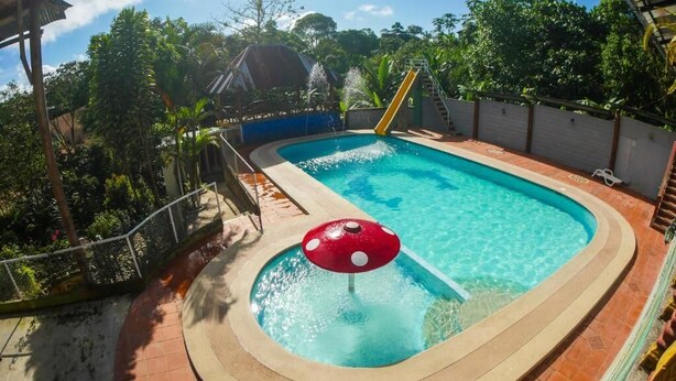 Una piscina con tobogán y un pequeño jacuzzi con una tapa en forma de hongo rojo.