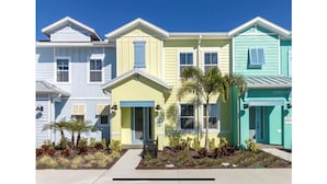 Une rangée de maisons de ville aux couleurs vives, chacune dotée d’un petit jardin devant et surplombant un ciel d’un bleu éclatant.