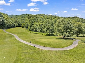 A golf course with a winding path, lush green grass, and dense forest in the background.