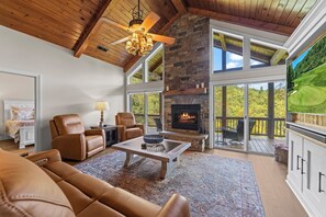 A spacious living room with a stone fireplace, leather furniture, and large windows offering a view of the outdoors. - Golf Course Views & Mountain Breezes - Your Perfect Condo Getaway (Whittier)