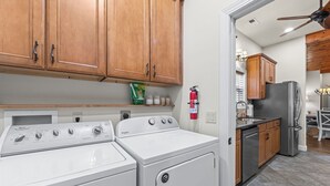 Eine Küche mit Holzausstattung, einer Whirlpool Waschmaschine, einem Whirlpool Trockner, einem Edelstahlkühlschrank und einem an der Wand befestigten Feuerlöscher.
