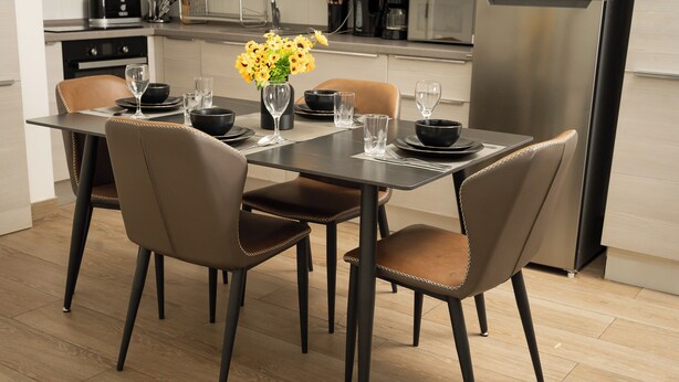 Un coin repas moderne avec une table sombre, quatre chaises et un vase rempli de fleurs jaunes.