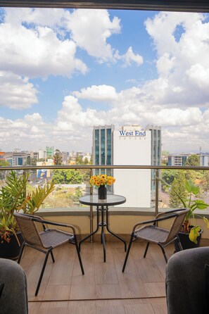 Un balcone con due sedie in vimini, un tavolino rotondo con un vaso di fiori e vista sullo skyline cittadino, inclusi i West End Towers.
