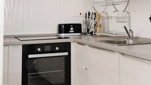 Une cuisine moderne avec des meubles blancs, un four noir, des plans de travail en acier inoxydable et une hotte noire.