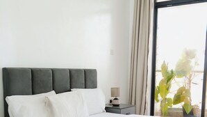 Une chambre moderne avec un grand lit, une table de chevet, une commode et une fenêtre avec des rideaux.
